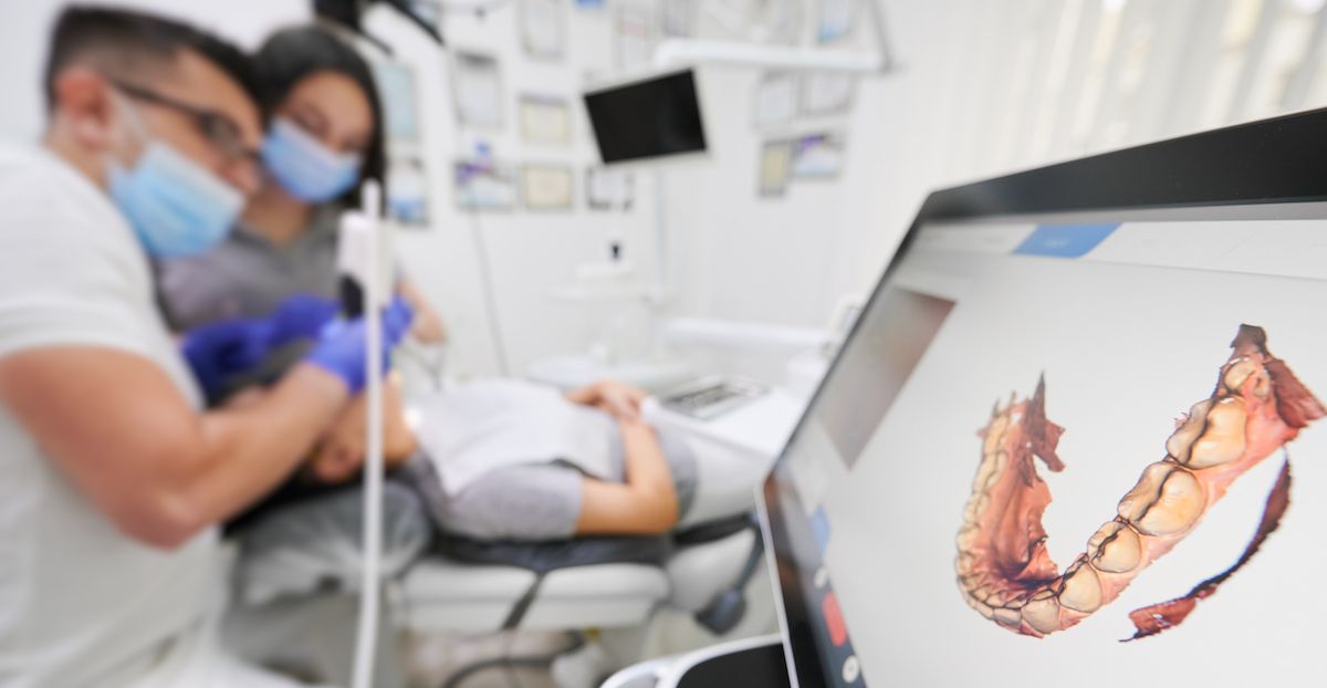 Zwei Kieferorthopäden untersuchen mit einem 3D-Scanner den Unterkiefer eines Patienten.