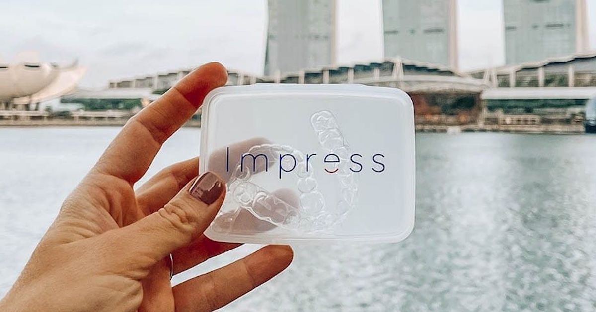 Onzichtbare Impress-aligners in hun etui met een stad op de achtergrond&nbsp;