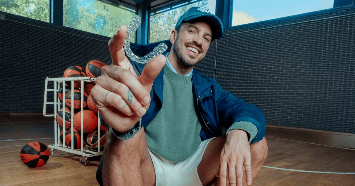 Un chico sostiene alineadores invisibles en su mano en un campo de baloncesto con pelotas de fondo.