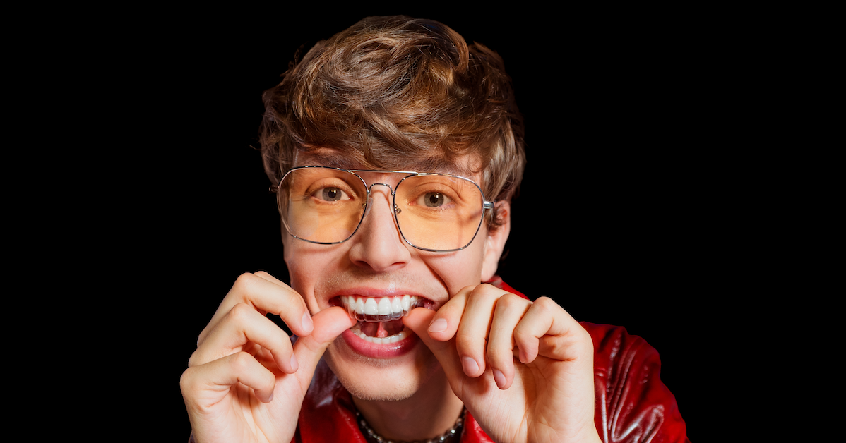 Chico está colocando sus alineadores invisibles con sus pulgares sobre fondo negro.