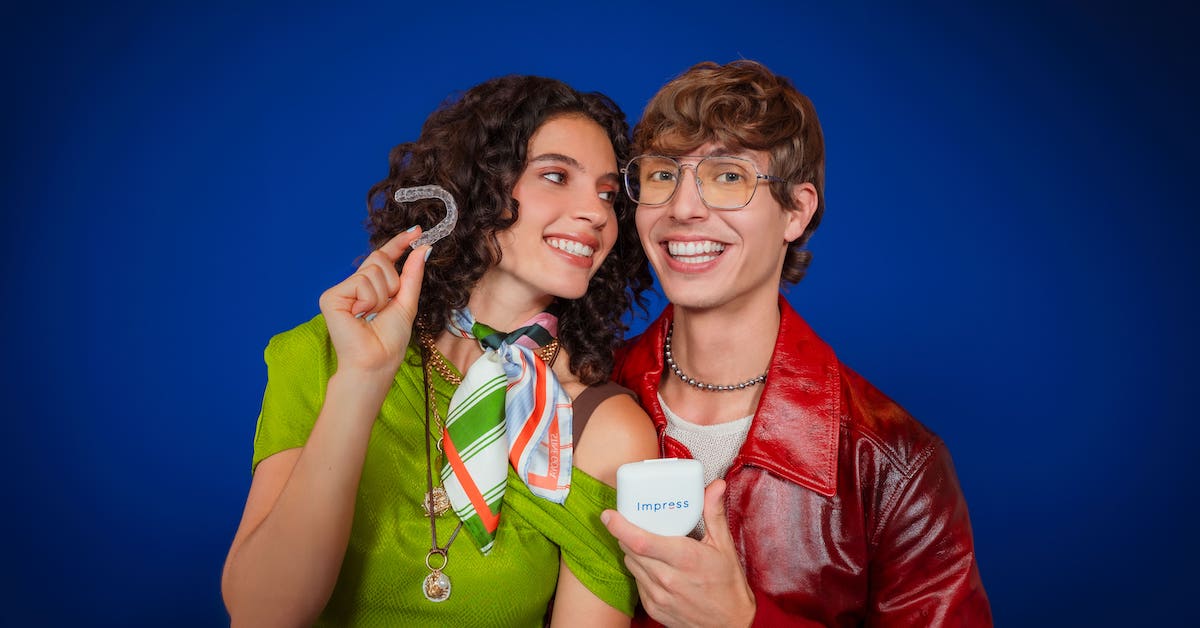 Una chica y un chico sobre fondo azul muestran un alineador dental Invisalign y la caja de Impress.