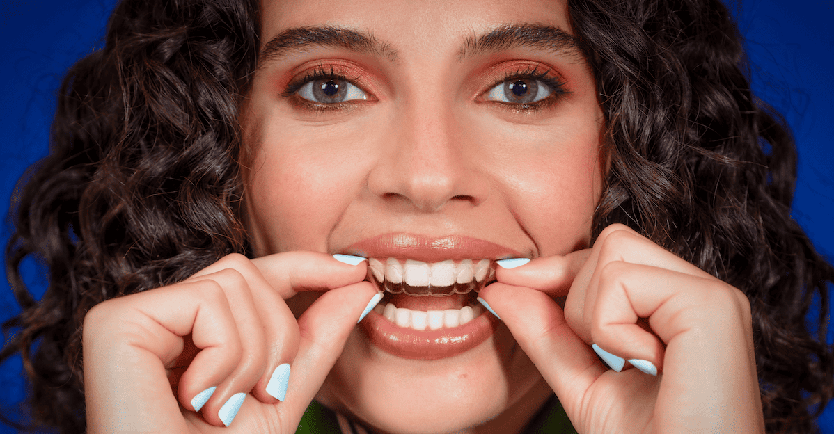 Chica sonriendo mientras sostiene un alineador invisible Invisalign®.