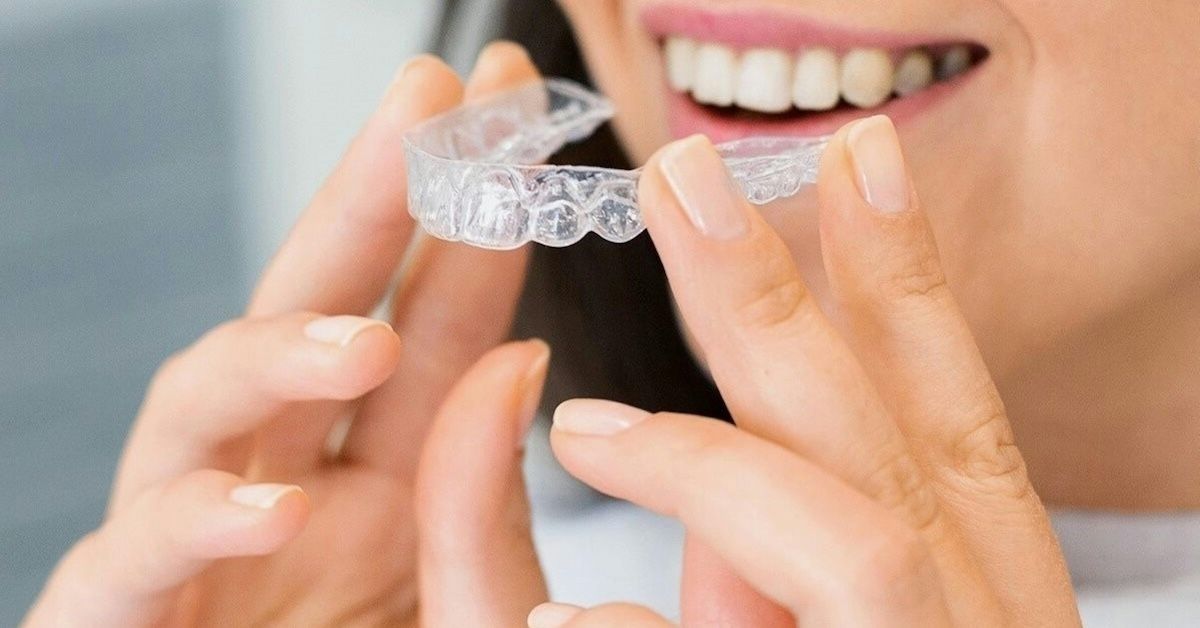 Une femme tient un aligneur dentaire transparent devant ses dents.