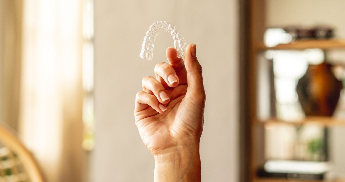 A hand holds an Impress clear aligner.&nbsp;