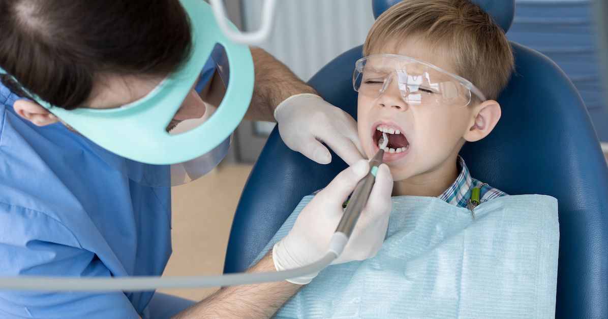 Een jongen met een angstig gezicht terwijl de tandarts zijn mond onderzoekt.&nbsp;