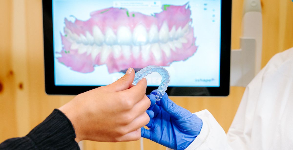 Doctor handing a patient an aligner with their 3D scan in the background.