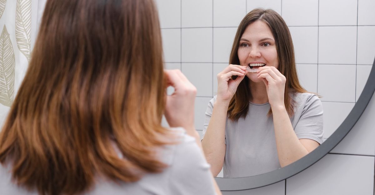 Mädchen, das vor einem Spiegel unsichtbare Aligner anlegt.