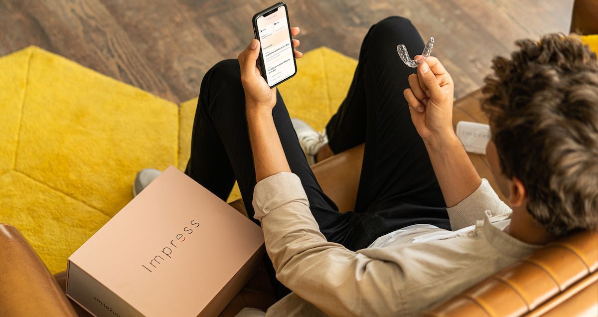 Een man houdt een aligner in de ene hand en een telefoon met de Impress-app in de andere hand.