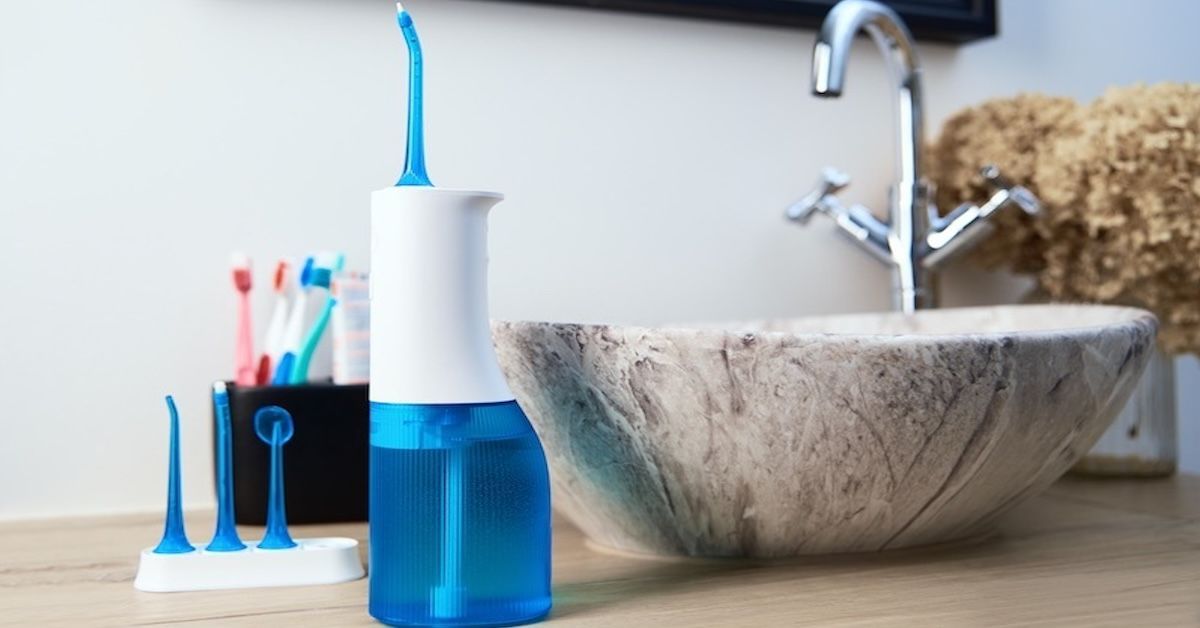 Een blauw-witte draagbare waterflosser met drie extra opzetstukken op een badkamerblad.