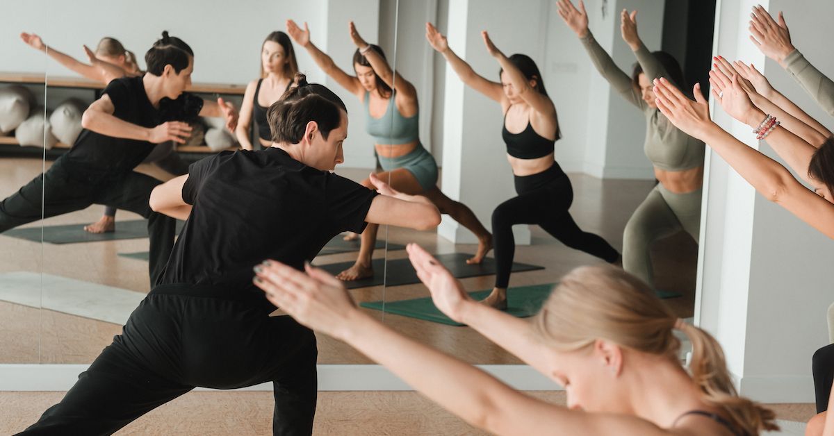 Un grupo de personas haciendo yoga en una sala con espejos. 