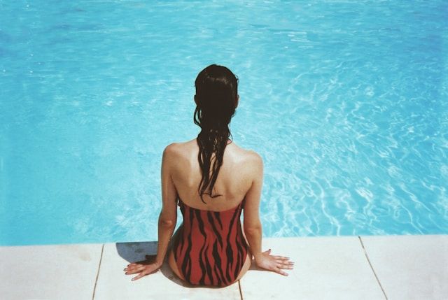 Frau sitzt im Badeanzug am Rand eines Pools.