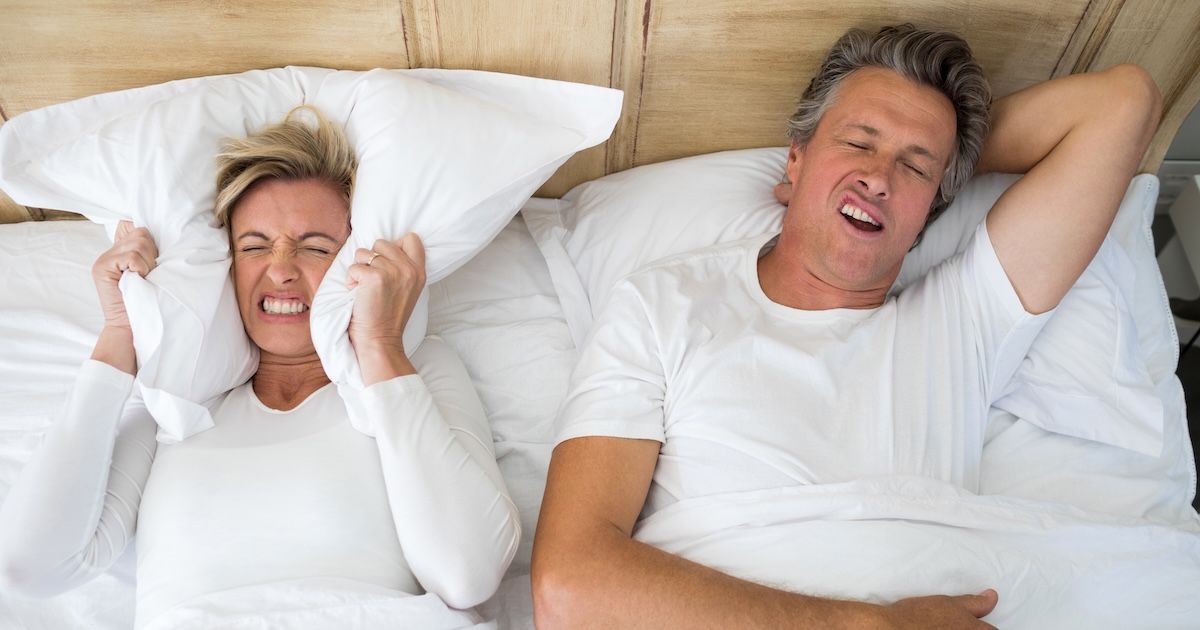 Een man die snurkt en een vrouw die haar kussen op haar oren houdt.
