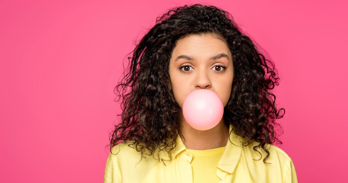 een vrouw die een bel blaast met kauwgom in haar mond