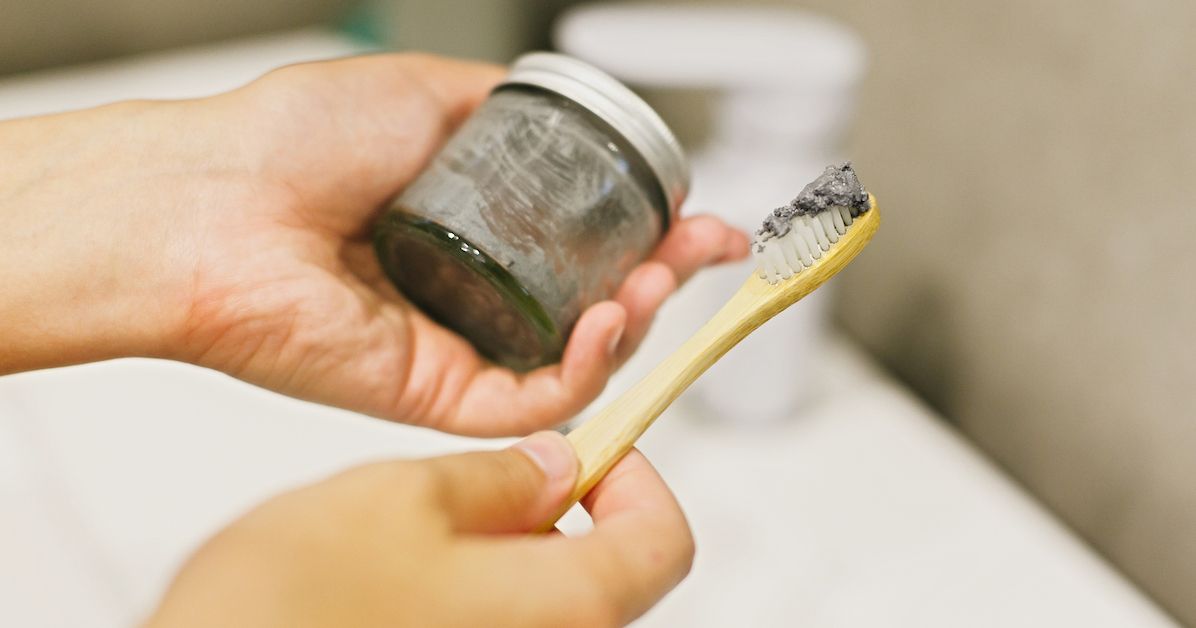 Una mano que sostiene un bote con pasta de dientes natural casera y un cepillo de dientes.&nbsp;