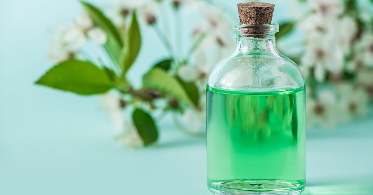 Un bote de cristal con un líquido verde de esmalte bucal natural dentro y flores de fondo.