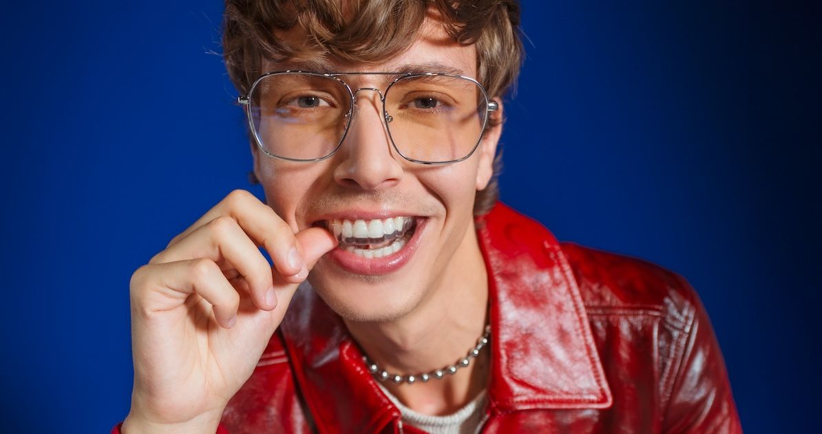 Jongen plaatst zijn onzichtbare aligners met zijn duimen met blauwe achergrond
