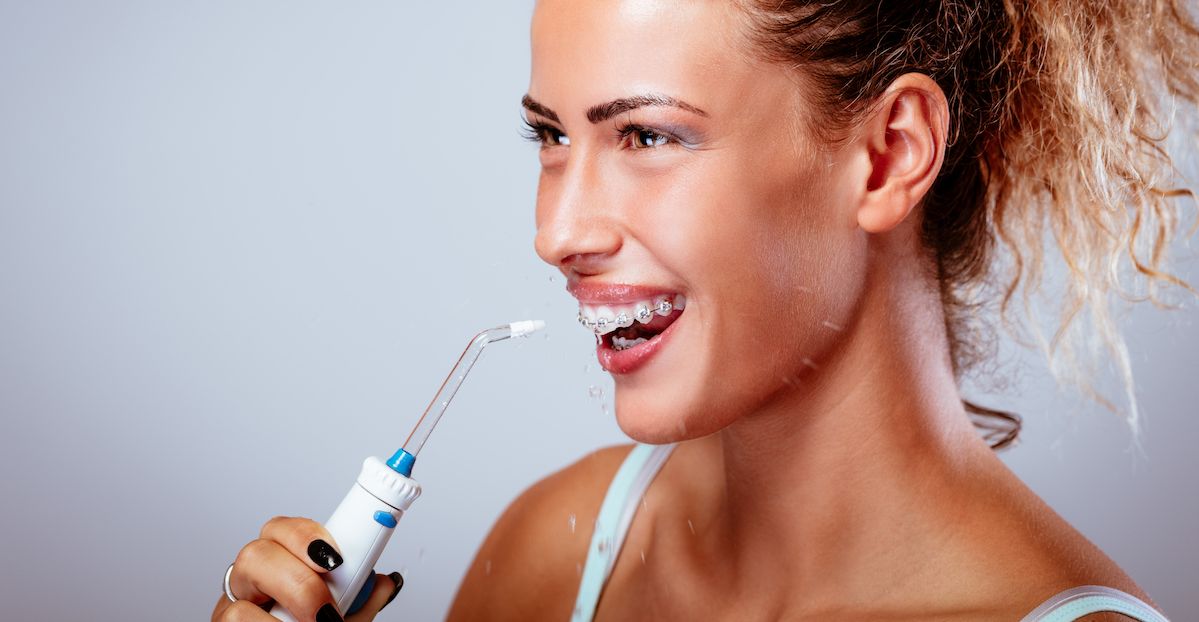 Mujer con brackets usando un irrigador de agua para limpiar los dientes.