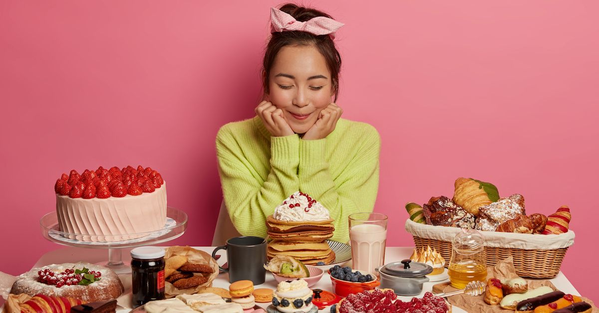 Chica sobre fondo rosa con muchos alimentos en una mesa para saber si se puede comer con el&nbsp;Invisalign®.