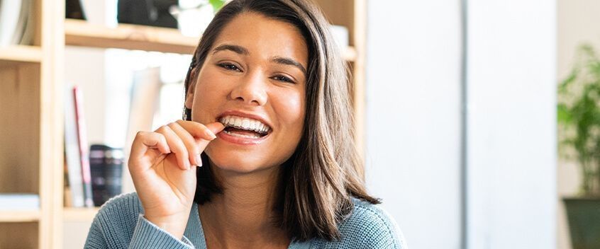 Een vrouw die glimlacht terwijl ze naar haar doorzichtige beugels wijst&nbsp;