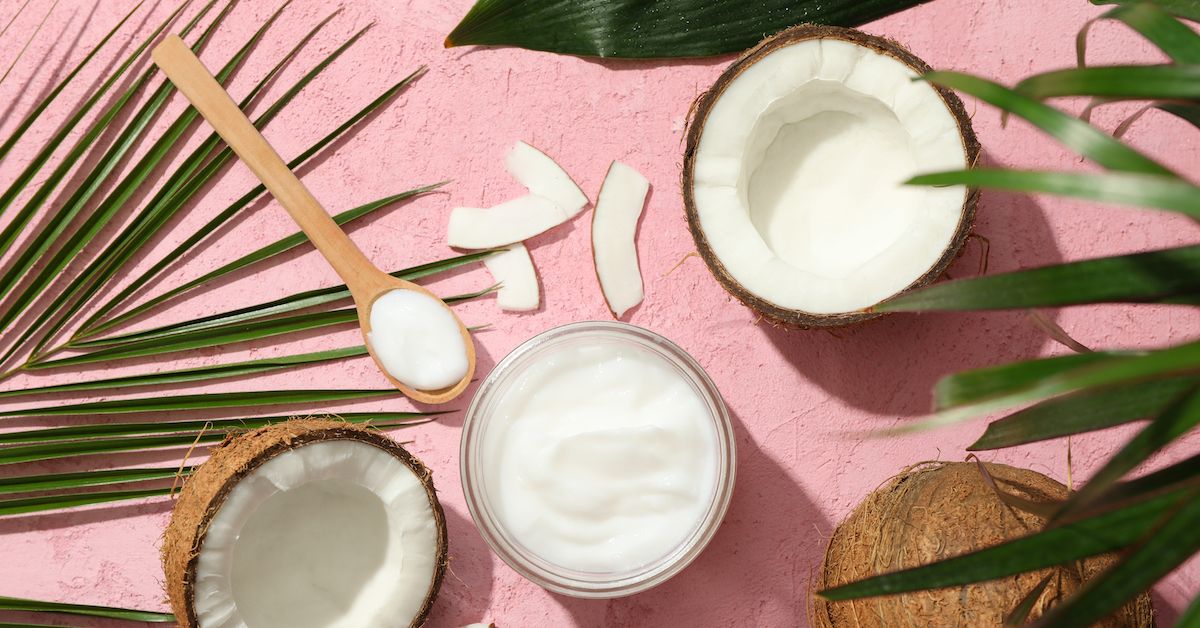 Bodegón con cocos partidos por la mitad, crema, hojas de palmera y trozos de coco.
