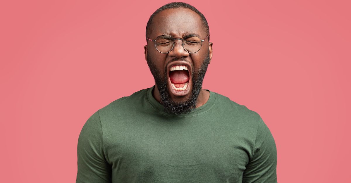 Hombre sobre fondo rosa que abre la boca mucho simulando una mordida abierta.