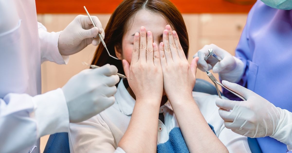Woman in dentist chair covering her face