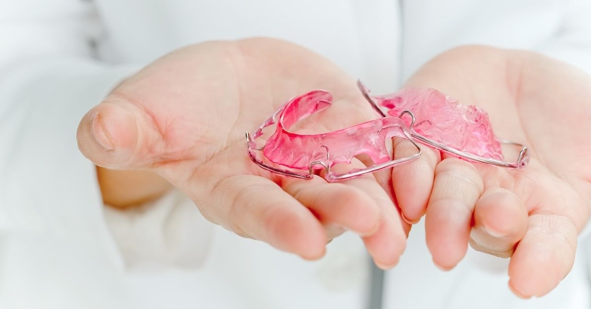 A dentist holding a removable Hawley retainer