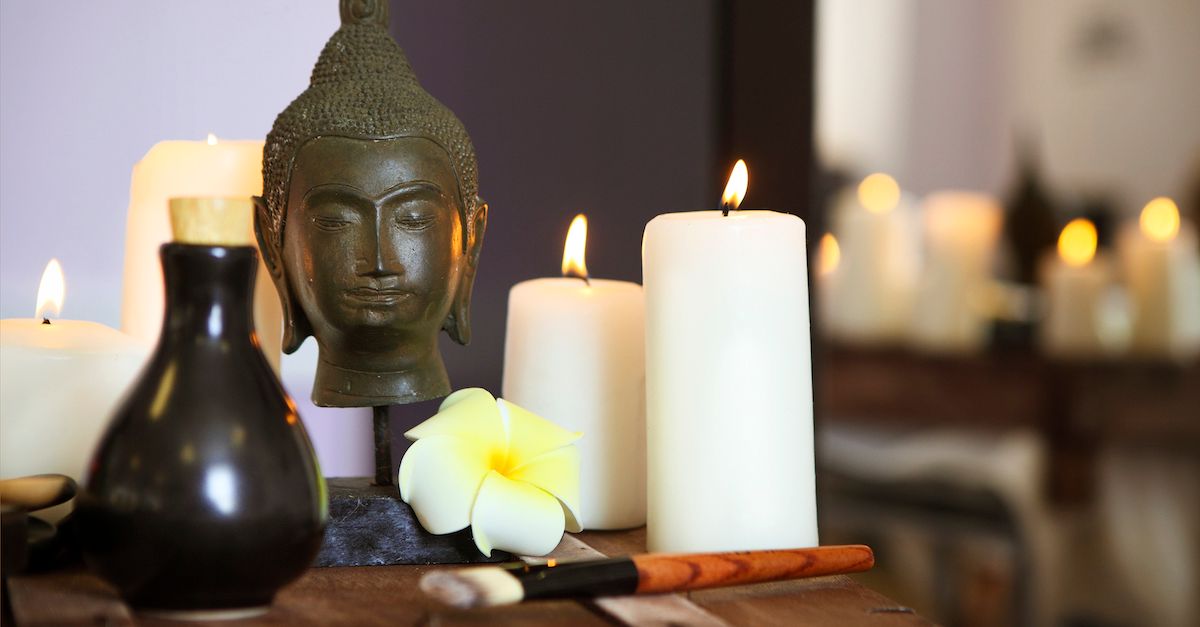 Un bodegón de velas, flores, aceites esenciales y una cabeza de Buda representando el ayurveda.
