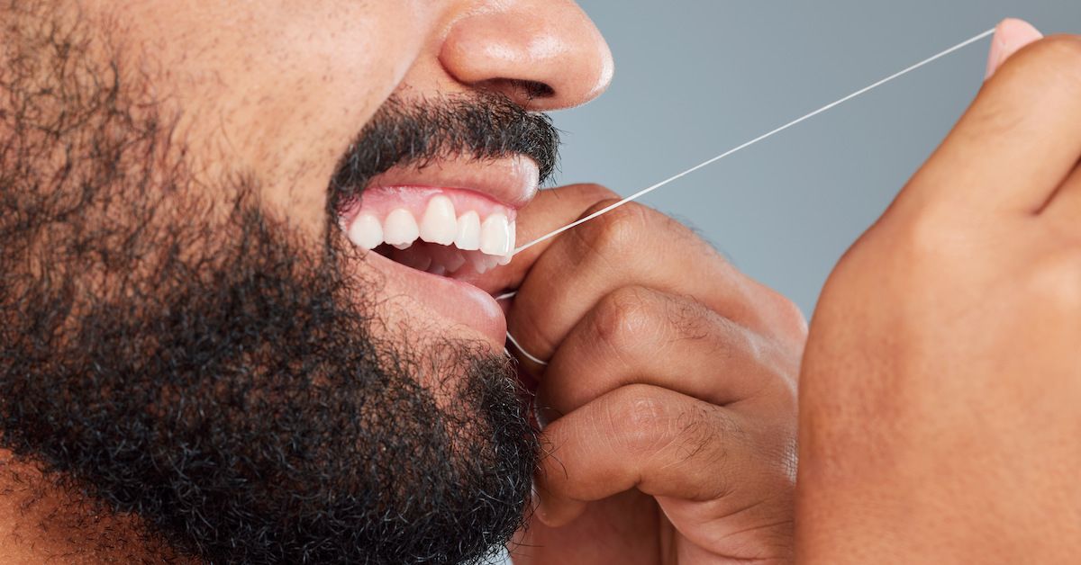Plano detalle de una boca de hombre con barba que pasa hilo dental en sus dientes.
