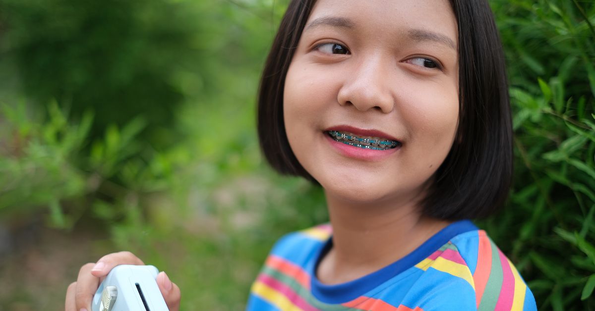 Una niña entre árboles sonríe mostrando los brackets metálicos de color azul.
