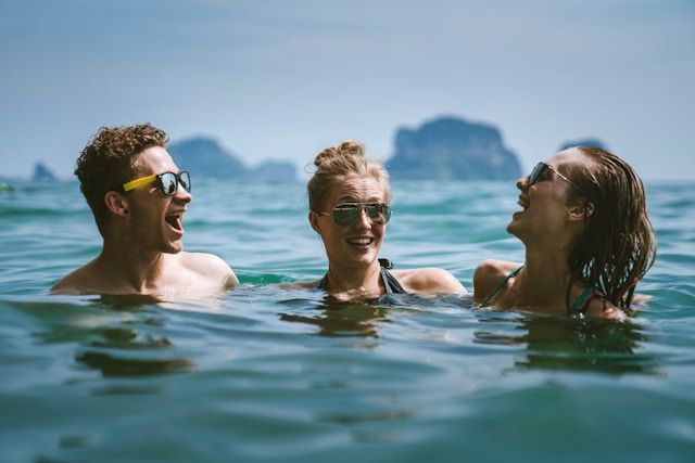Zwei Frauen und ein Mann schwimmen im Meer und lachen.