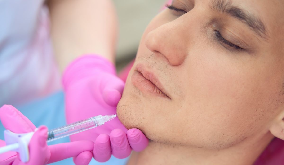 junger Mann bekommt eine Spritze ins Kinn mit Hyaluron Filler