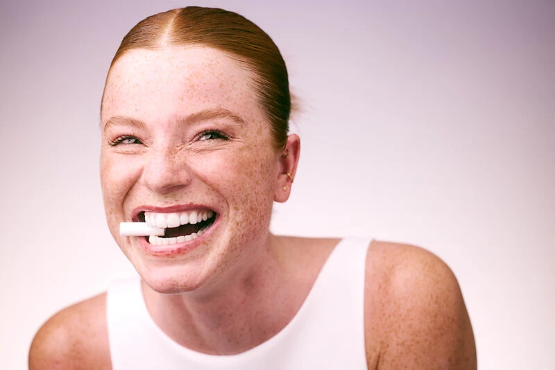 junge Frau hat einen Chewie im Mund und lacht in die Kamera