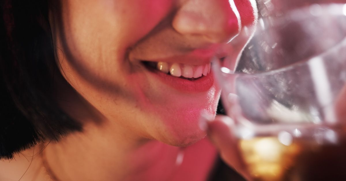 eine junge Frau die lächelt, während sie ein alkoholisches Getränk in der Hand hält