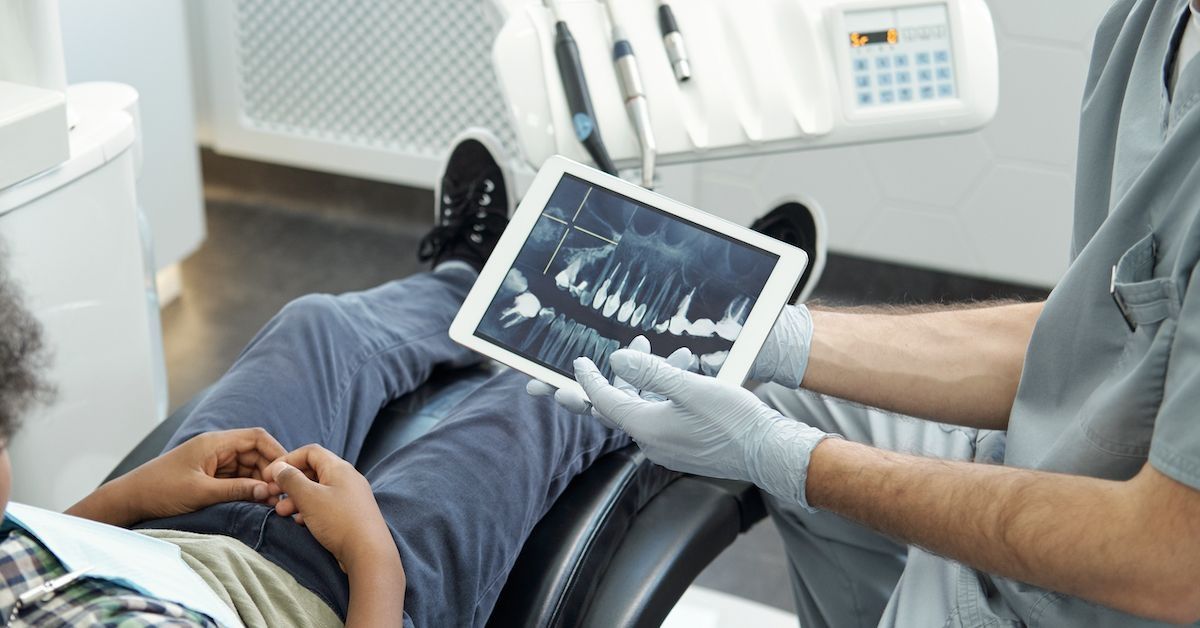 Tandarts die een jonge patiënt een röntgenfoto van het gebit laat zien.