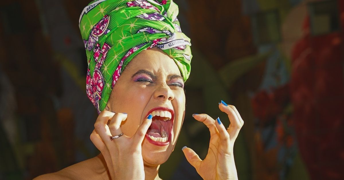 Vrouw met een groene hoofddoek, schreeuwt met open mond en gebaart met haar handen.&nbsp;