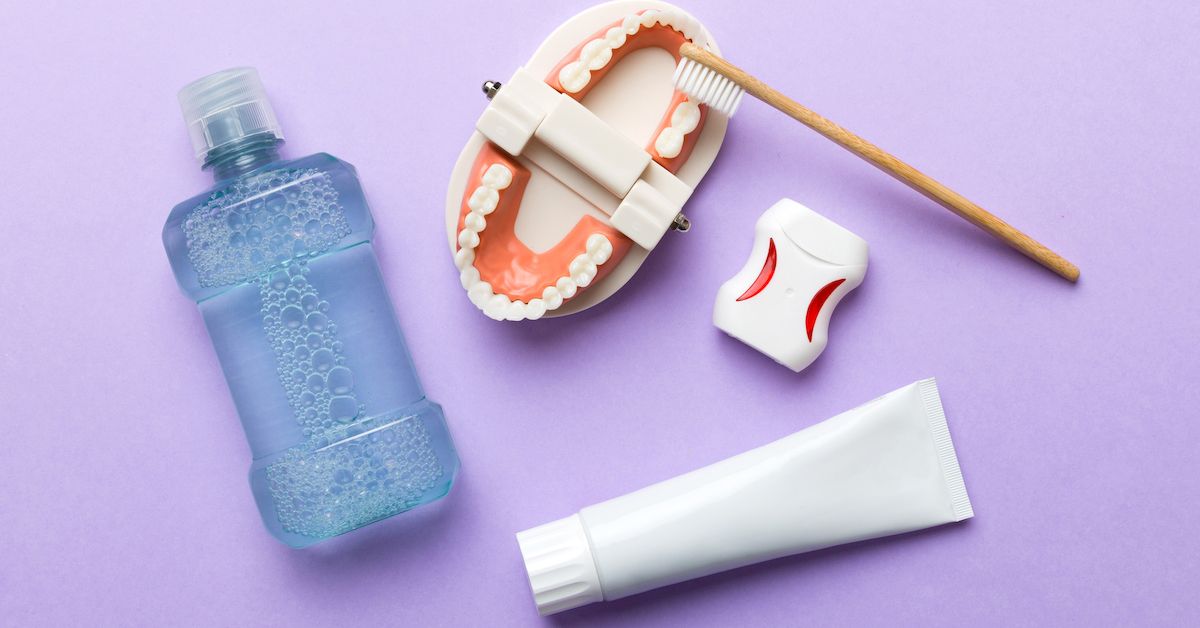 Colutorio, cepillo, hilo y pasta dental sobre fondo lila para hacer un blanqueamiento casero.