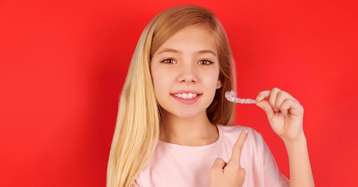 Una niña sujeta unos alineadores invisibles sobre fondo rojo.