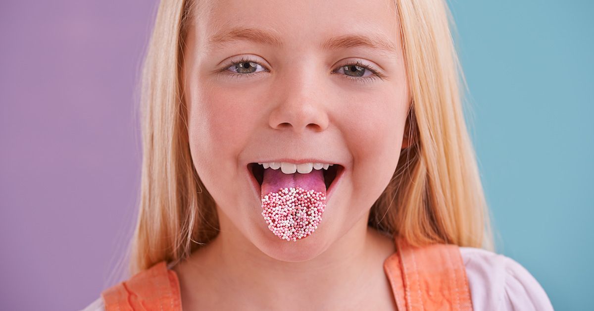 Una niña con bolitas pequeñas blancas en la lengua. Son gominolas que simulan un virus.