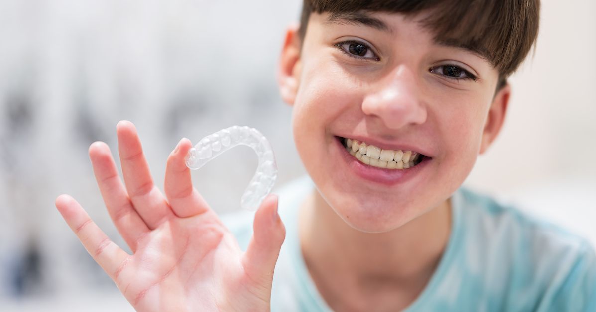 Un adolescente muestra su alineador invisible y lo alineados que están sus dientes.