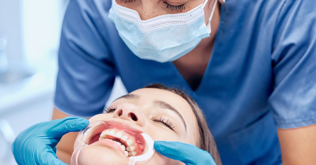 Un dentista sujeta el abrebocas dental de la paciente en su boca.
