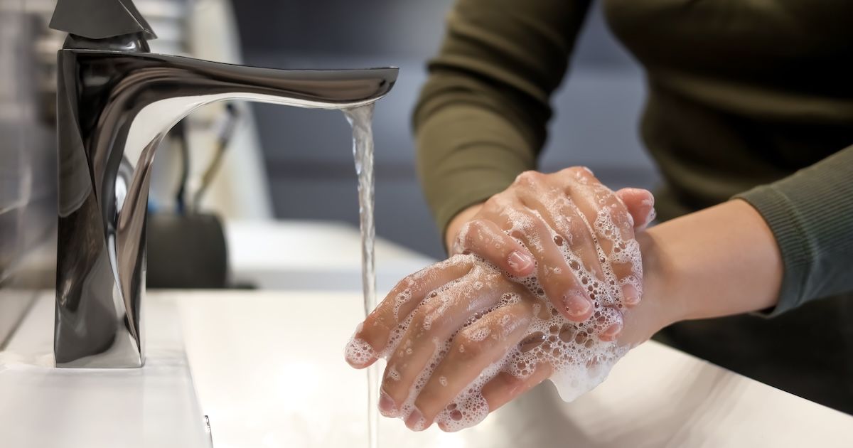 Handen worden onder de lopende kraan in een wasbak gewassen.
