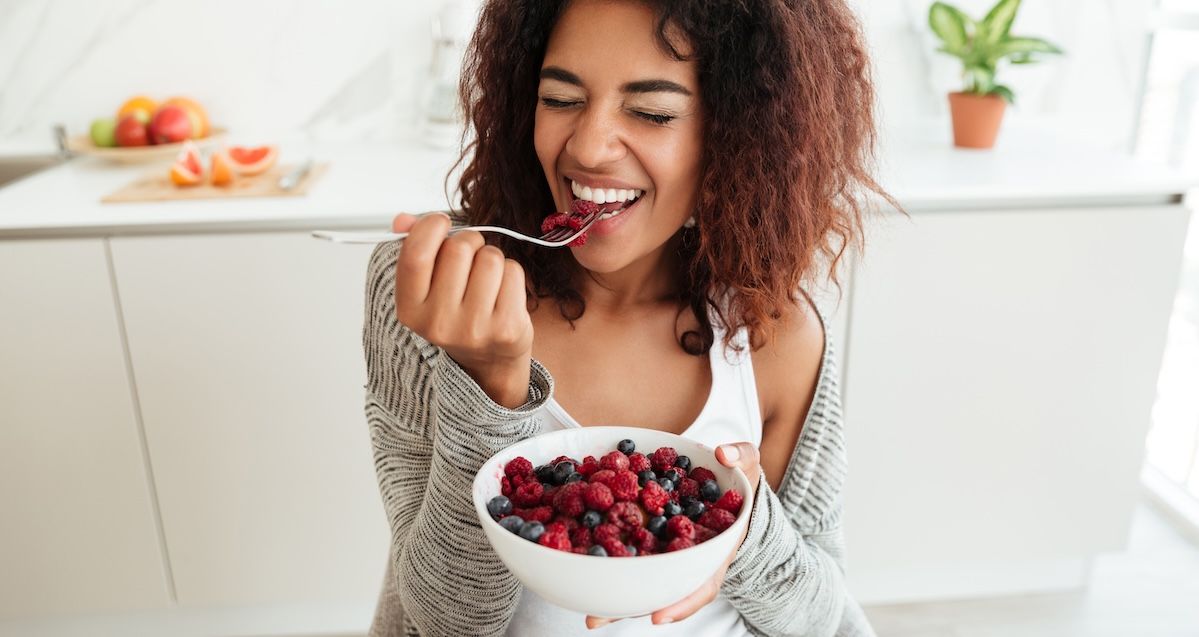 Een vrouw die blij haar bakje rood fruit eet