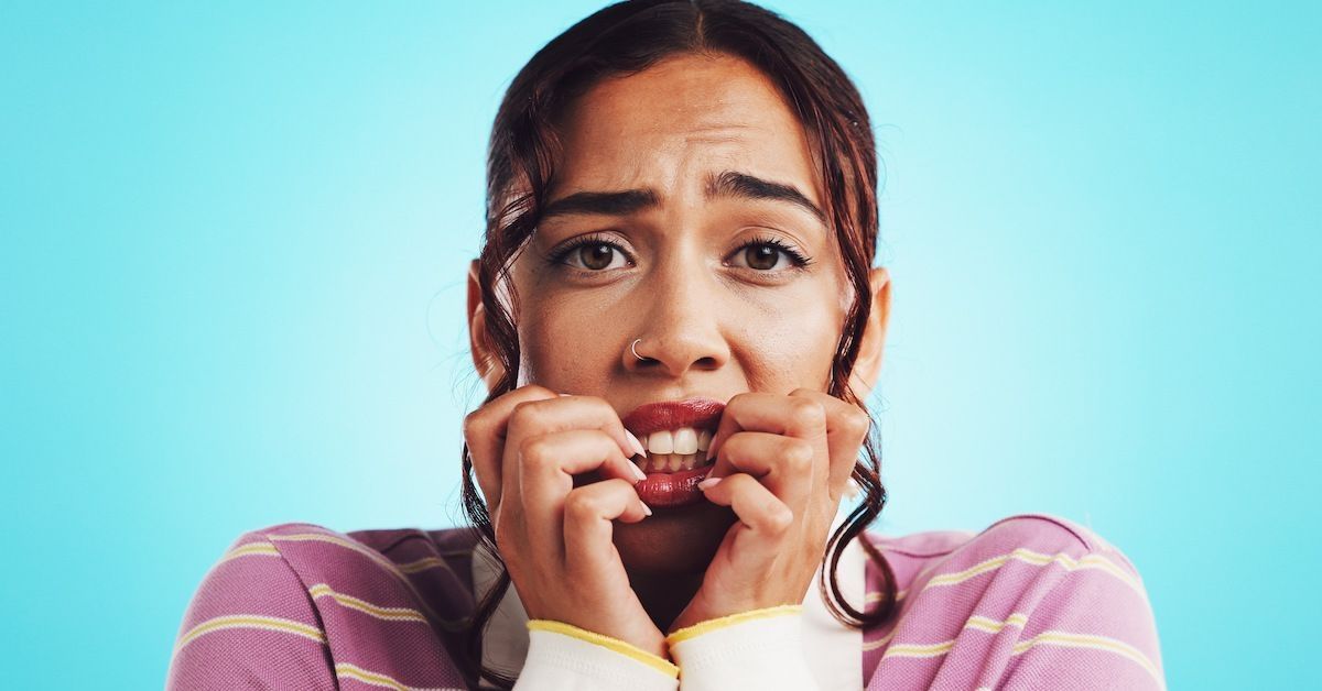 Meisje dat op haar nagels bijt tegen een blauwe achtergrond met een roze gestreepte trui.&nbsp;