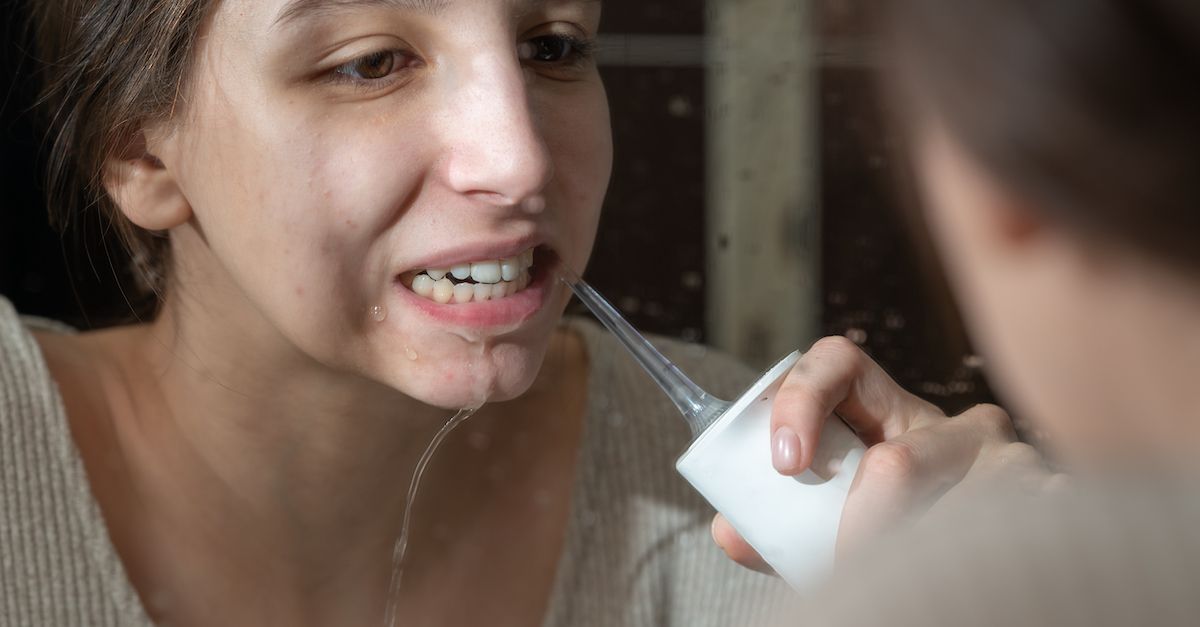 Una ragazza si guarda allo specchio mentre usa l'idropulsore dentale.