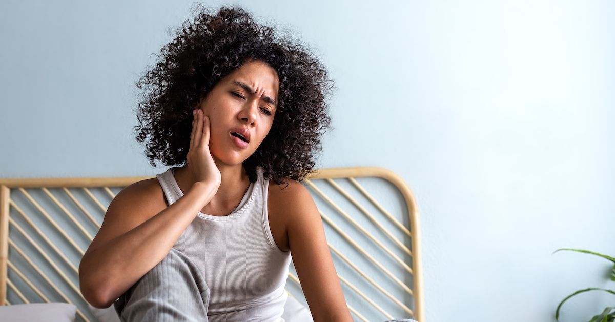 Una mujer que se toca la mandíbula como signo de dolor por bruxismo.
