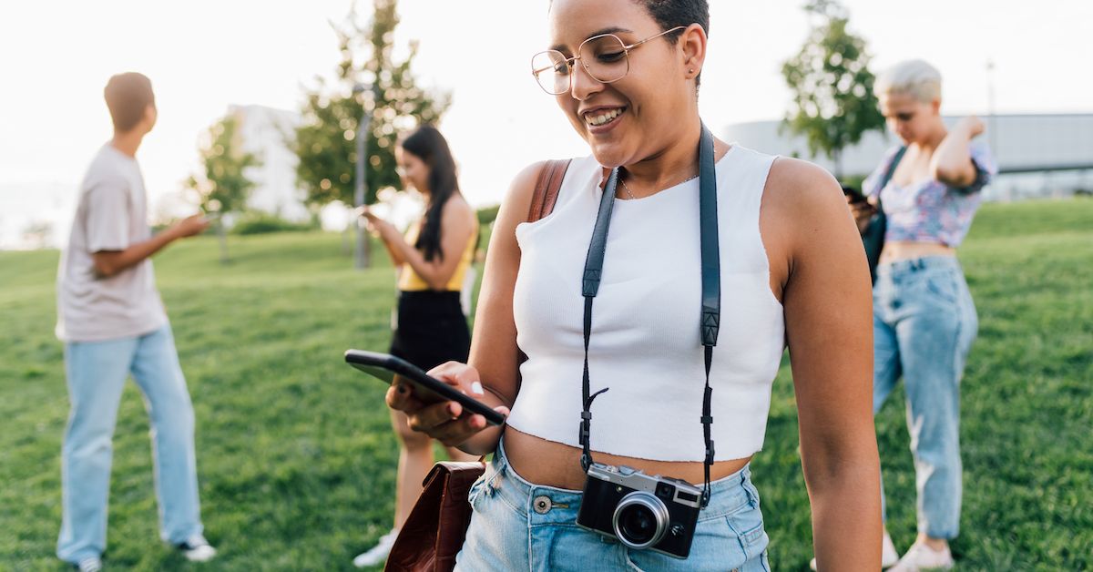 Unos cuantos adolescentes en el césped miran sus móviles como haciendo ver que están mirando la app de Impress para su tratamiento Invisalign® para adolescentes.